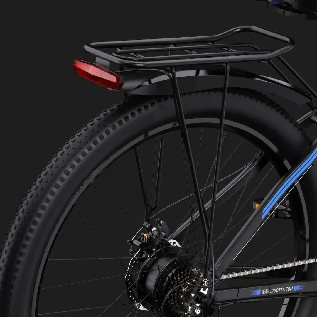 Izdelek na sliki je električno kolo znamke Duotts, model C29. Na sliki je vidna zadnja stran kolesa z nosilcem za prtljago in rdečo lučjo, kar nakazuje na funkcionalnost za prevoz in varnost. Kolo ima široke gume, kar je značilno za terenska kolesa.