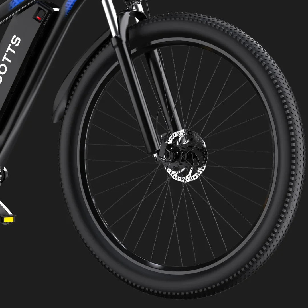 Izdelek na sliki je električno kolo znamke Duotts, model C29. Na sliki je vidna sprednja kolesa s širokimi gumami in disk zavornim sistemom, kar kaže na robustno zasnovo, primerno za različne terene. Kolo ima tudi elegantno črno barvo in sodoben dizajn.