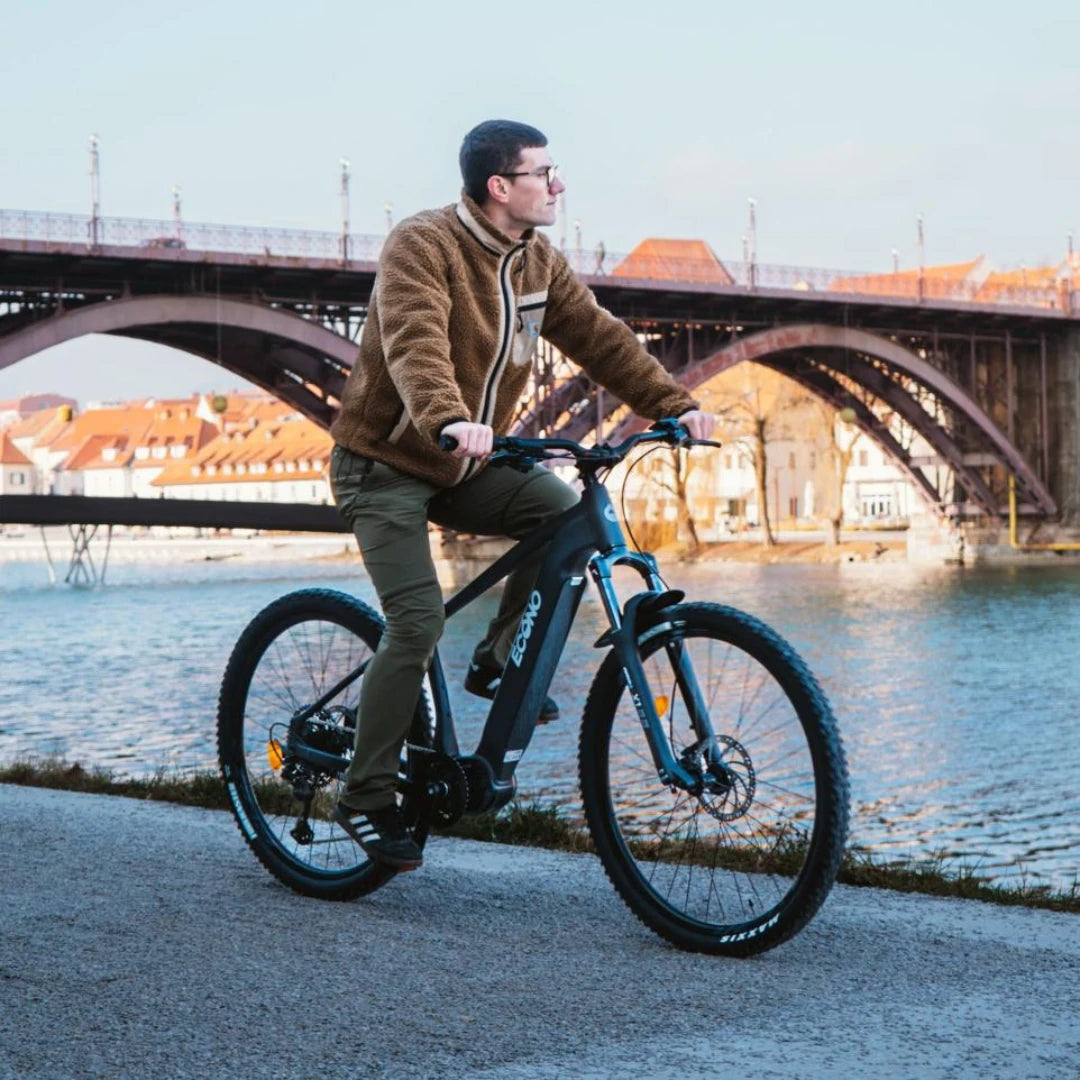 Electric Bike Econo Gams Suv C6, sleek design, rider on scenic riverside path, vintage bridge in background.