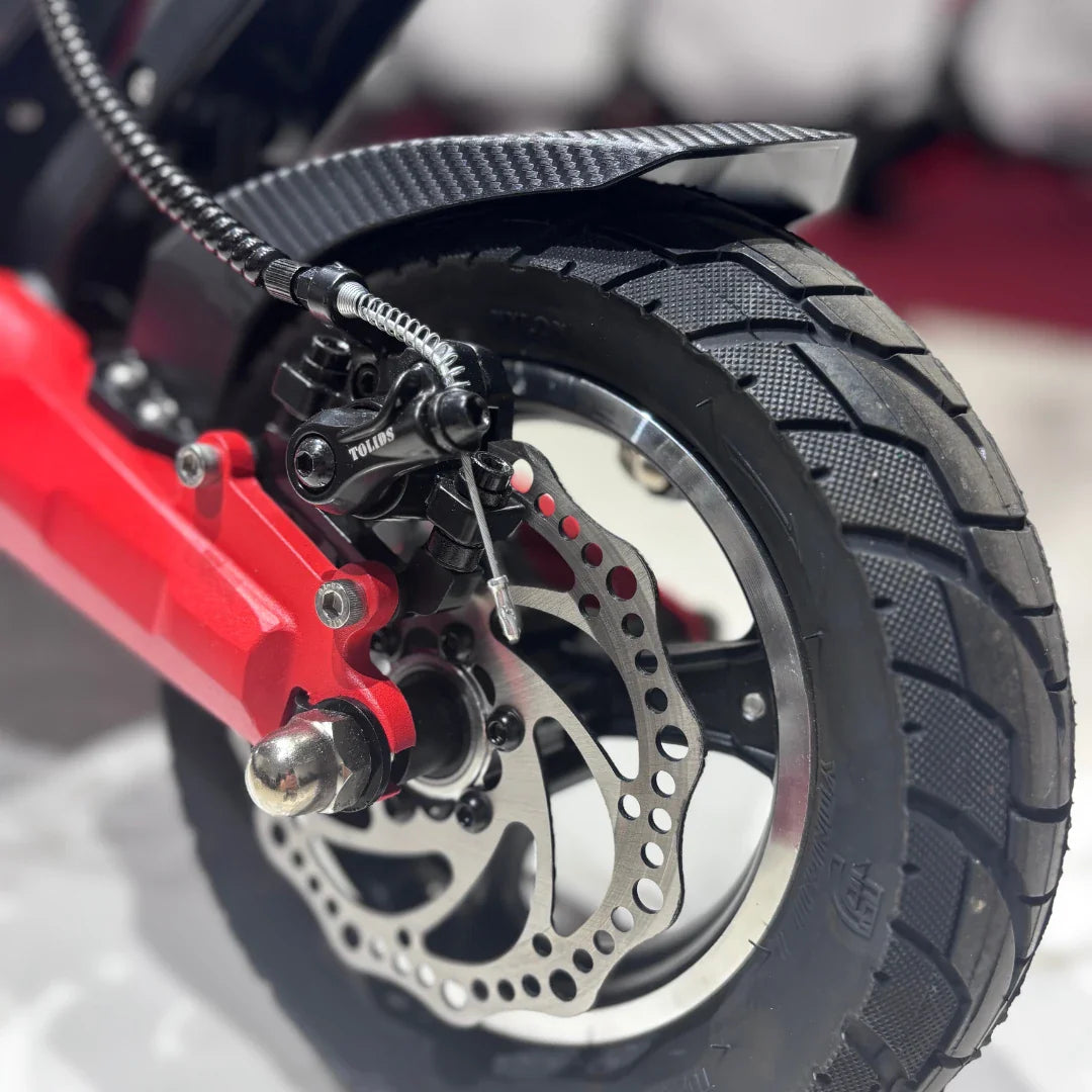 Izdelek na sliki je električni skiro, model Eco Speed 9. Vidna je zadnja kolesna enota, ki vključuje disk zavoro, gumijast kolesni obroč in del okvirja v rdeči barvi. Detajli, kot so vzmetenje in struktura kolesa, kažejo na robustno zasnovo, primerna za urbano vožnjo.