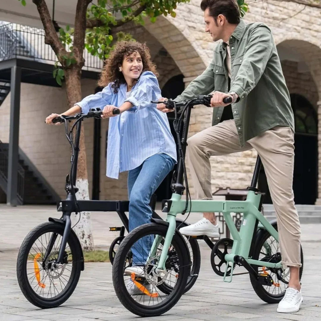 Na sliki je električno kolo znamke Engwe, model P20. Prikazani sta dve osebi, ki se zabavata na kolesih v urbanem okolju. Obe kolesi imata kompaktno zasnovo, z manjšimi kolesi in modernim videzom. Osebi sta oblečeni v sproščena oblačila, kar nakazuje, da se kolesarjenje dogaja v sproščenem vzdušju. V ozadju so vidne arhitekturne značilnosti, ki dodajajo mestni pridih.