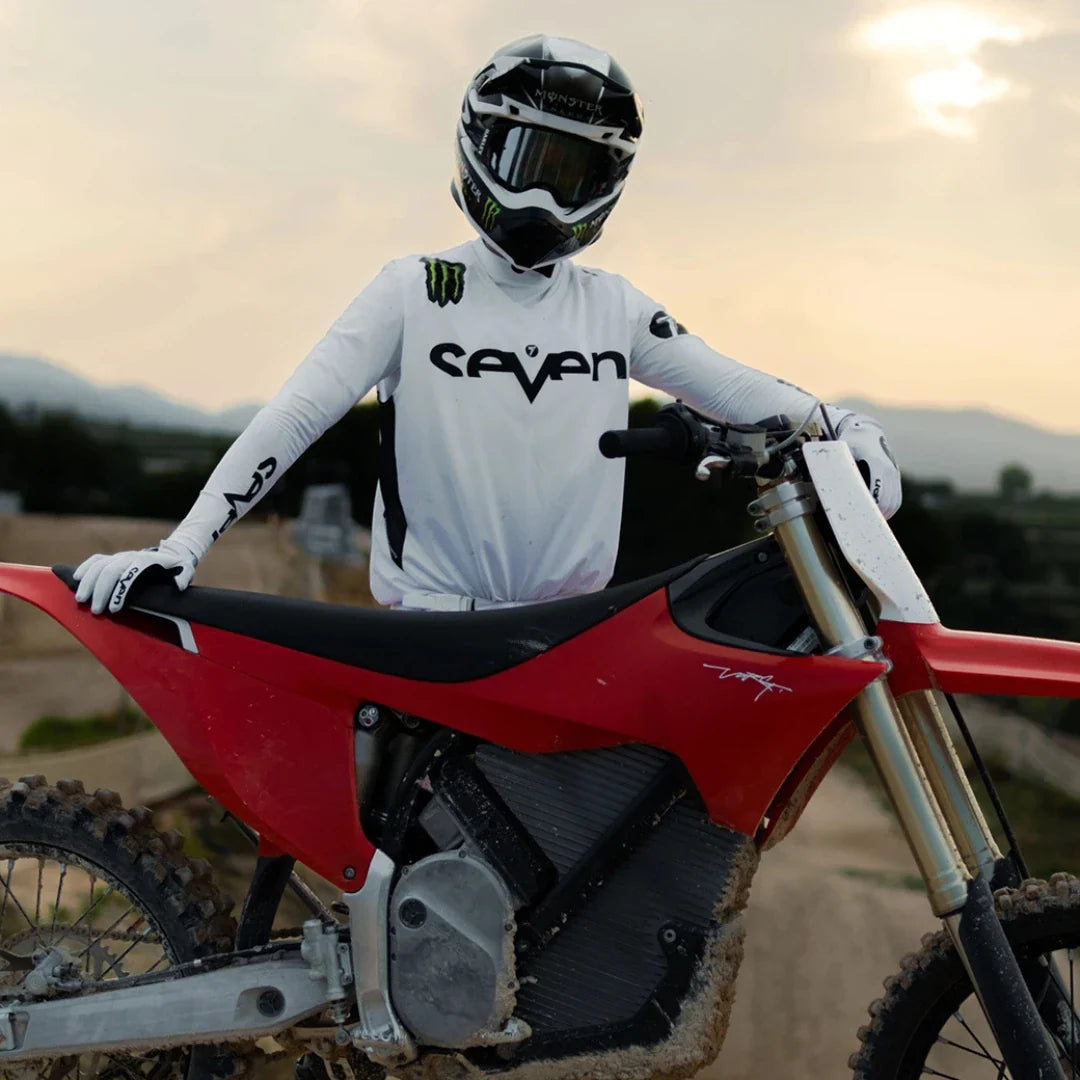 Jezdec stoji ob električnem motokros kolesu Stark Varg s sončnim zahodom v ozadju.