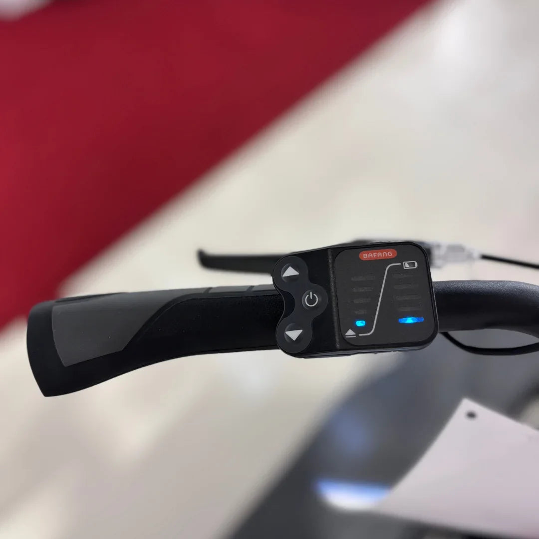 Izdelek je električno kolo, znamke Fischer, model Cita 1.0. Na sliki je prikazan del krmila, kjer so vidni gumbi za upravljanje ter indikatorji stanja baterije. Oprema je zasnovana za enostavno uporabo, kar omogoča udobno vožnjo.