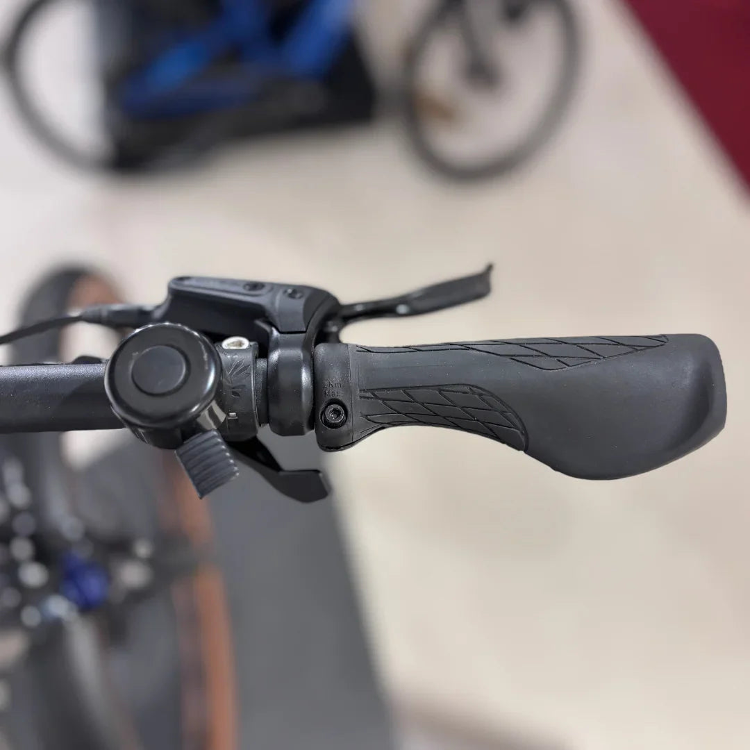 Izdelek na sliki je električno kolo, model Malaguti Carezza TR 4.0 High Step. Na sliki je prikazan del krmila, kjer so vidne ročice za prestavljanje in zaviranje ter gumijasti ročaji za boljši oprijem. Kolo ima sodoben dizajn, kar nakazuje na udobno in učinkovito vožnjo.