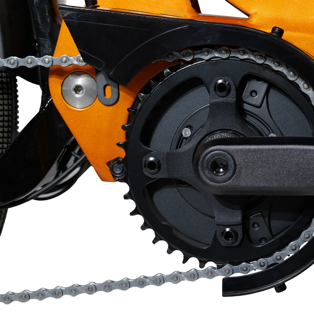 Izdelek na sliki je električno kolo, model MS Energy SUV C502. Na sliki je prikazan del pogonskega sistema, ki vključuje verigo in zobnik. Barvna kombinacija je črna in oranžna, kar daje kolesu dinamičen videz. Vidna je tudi struktura okvirja, ki je zasnovana za robustnost in stabilnost.