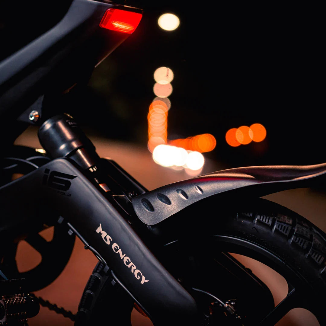 Izdelek na sliki je električno kolo, znamke MS Energy, model Urbanfold i6. Na sliki je prikazan zadnji del kolesa, kjer je vidna luč in del okvirja s logotipom MS Energy. Kolo ima športen dizajn in je primerno za urbano vožnjo, kar nakazuje tudi nočna osvetlitev v ozadju.