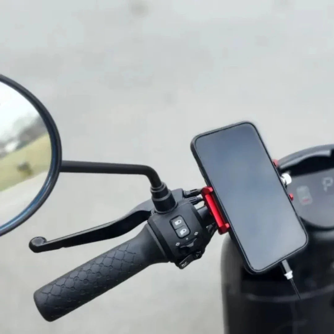 Na sliki je električna motorna kolesa, model "Stromko". Vidno je krmilo s črnim ročajem, na katerem je nameščen tudi nosilec za telefon. Telefon je povezan z napravo, kar nakazuje na možnost navigacije ali predvajanja glasbe med vožnjo. V ozadju je tudi ogledalo, kar prispeva k varnosti med vožnjo.