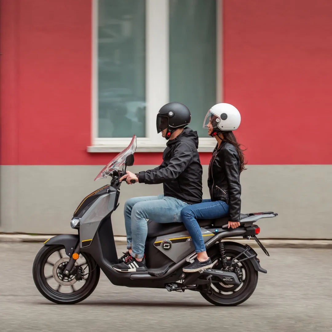 Par se vozi z električnim skuterjem Super Soco Cpx pred pisanim ozadjem stene.