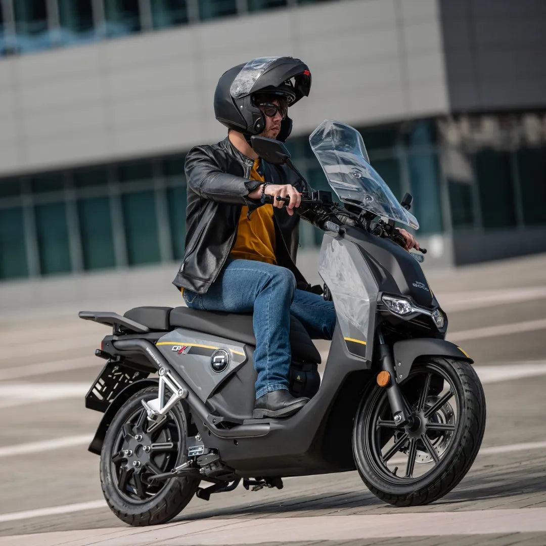 Voznik s čelado na električnem skuterju Super Soco Cpx v urbanem okolju.