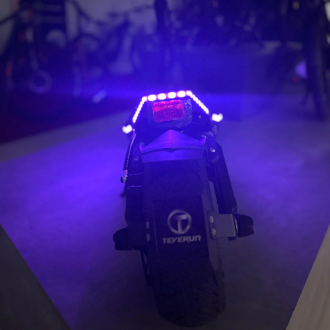 Na sliki je električni skiro, model Teverun Fighter Mini Pro 2025. Vidna je zadnja stran skiroja, ki ima močno svetlo in reflektor, kar povečuje vidnost. Opremljen je s širokimi gumami, kar nakazuje na stabilnost in udobno vožnjo. Znamka Teverun je jasno vidna na zadnjem delu skiroja.