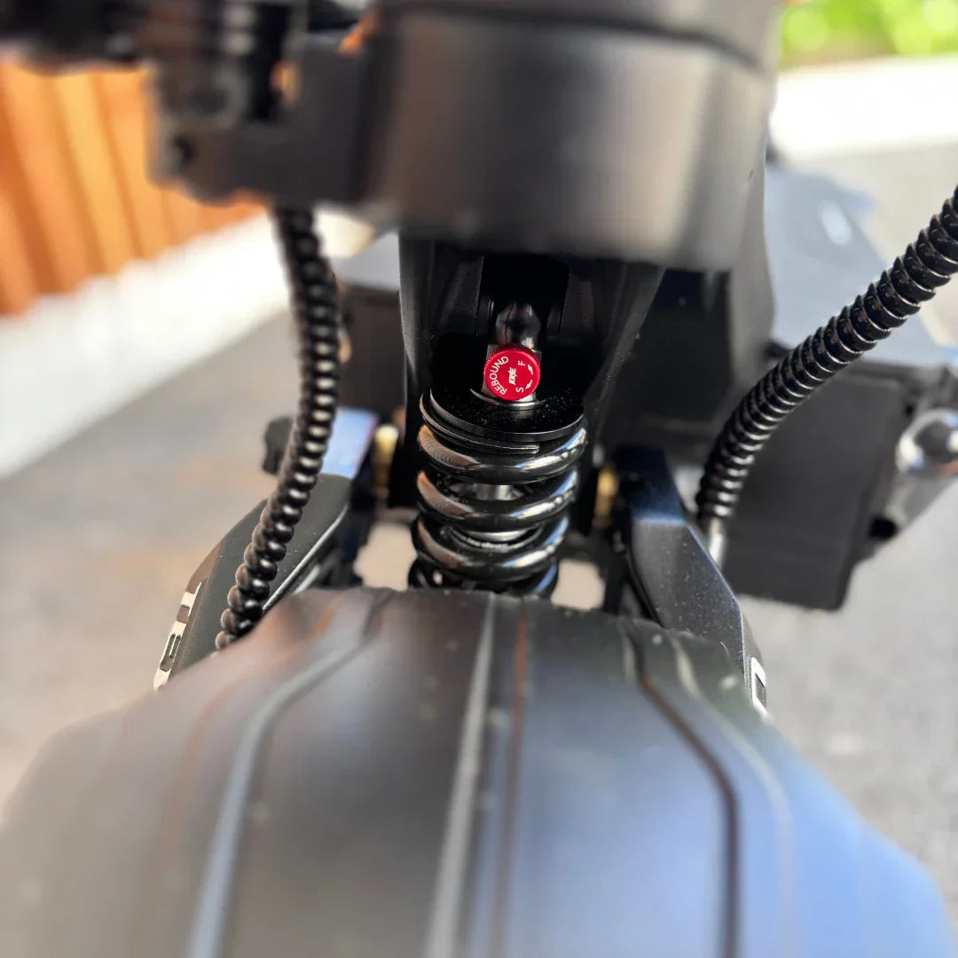 Izdelek je električni skiro, znamke Teverun, model Fighter Supreme 7260 Ultra. Na sliki je vidna podrobnost vzmetnega sistema, ki vključuje črno vzmet in rdeč indikator, ki označuje nastavitev. V ozadju se vidi del strukture skiroja, kar nakazuje na robustno zasnovo.