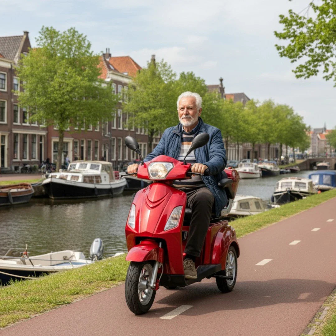 Izdelek na sliki je električni mobilni skuter s tremi kolesi, model Vigorous Vista 1. Na sliki je videti starejšega moškega, ki vozi rdeč skuter po poti ob kanalu, obdanim z drevesi in hišami. V ozadju so vidne tudi čolne, kar ustvarja prijetno mestno vzdušje.