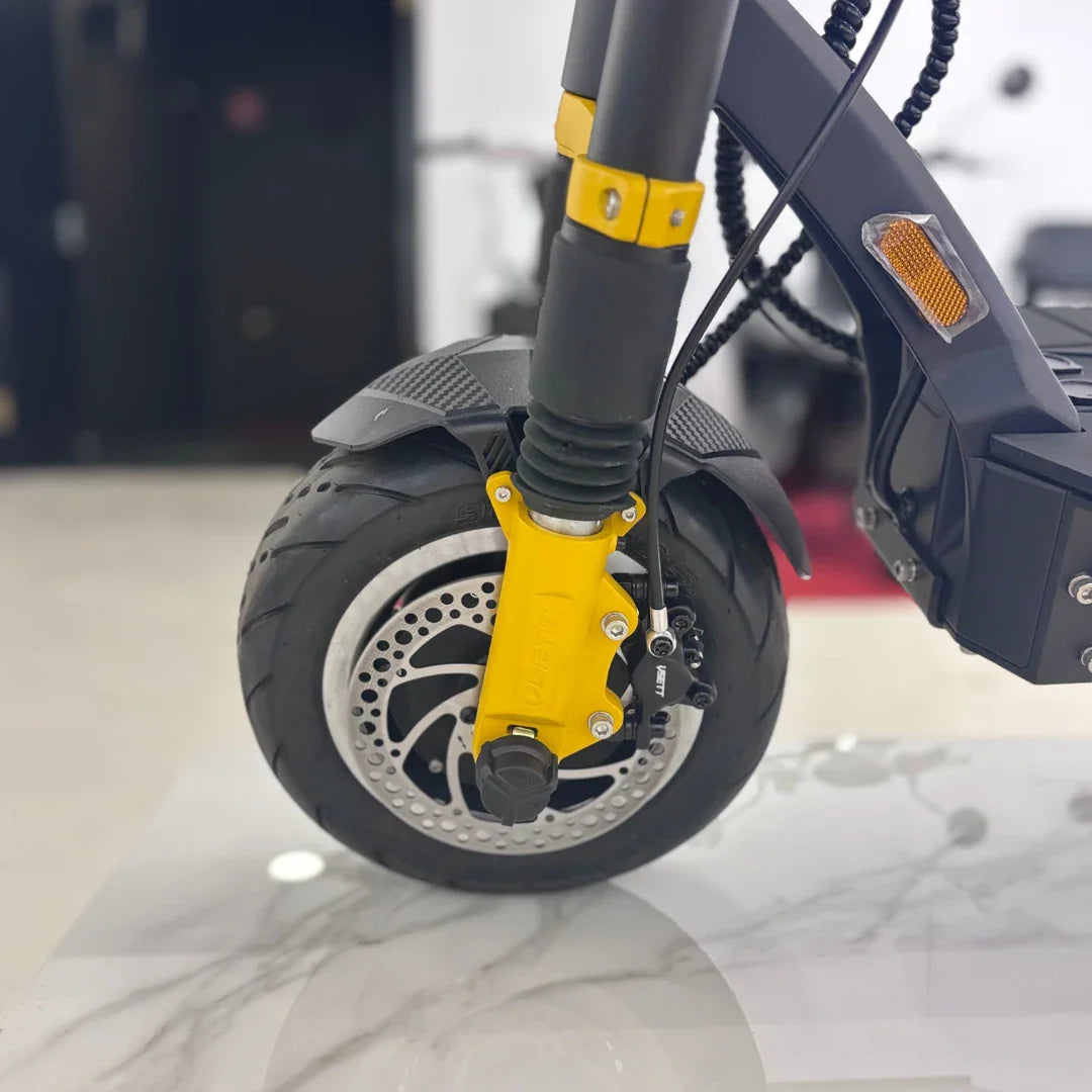 Na sliki je električni skiro znamke Vsett, model 11 Super. Vidna je sprednja pnevmatika s športnim profilom ter rumena vilica, ki nudi dodatno stabilnost. Na sliki so tudi zavorni sistem in disk, kar kaže na dobro zmogljivost in varnost pri vožnji. Ozadje je nejasno, kar omogoča osredotočenost na izdelek.