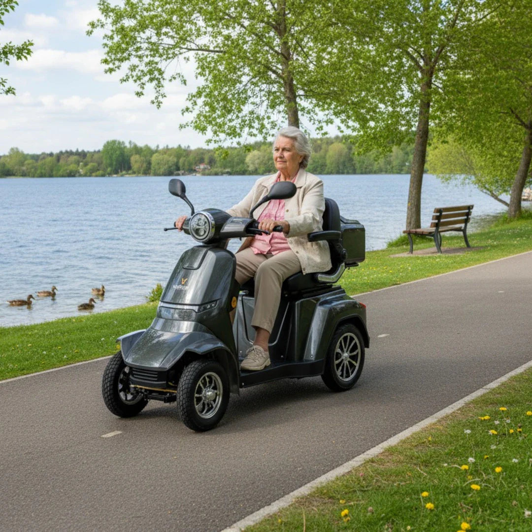 Izdelek je električni skuter, znamke Veleco, model Gravis. Na sliki vidimo starejšo osebo, ki vozi skuter ob jezeru, obdanem z zelenjem in drevesi. Skuter ima tri kolesa, kar zagotavlja stabilnost, in je zasnovan za udobno vožnjo. V ozadju so vidne tudi klopi in ptice, kar ustvarja prijetno naravno okolje.