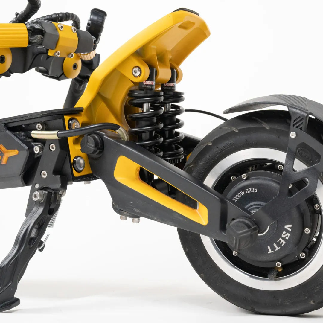 Izdelek na sliki je električni skiro, model Vsett 11 Super. Vidna je zadnja stran skiroja, kjer so prikazani amortizerji in zadnje kolo. Barvna kombinacija je črna in rumena, kar daje skiroju dinamičen videz. Amortizerji so zasnovani za boljšo udobnost pri vožnji, kar je pomembno za uporabo na različnih terenih.