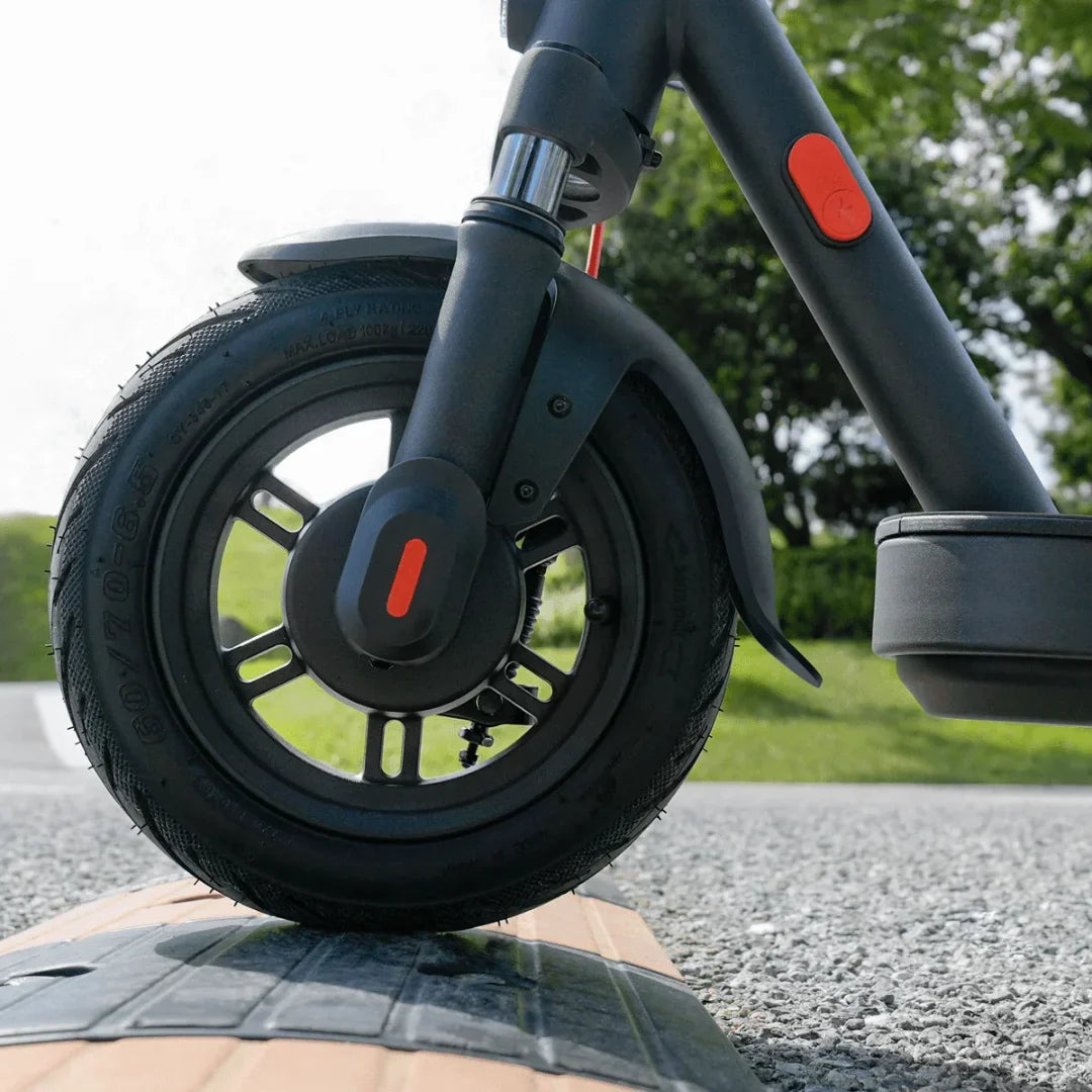 Izdelek je električni skiro znamke Xiaomi, model Elite. Na sliki je prikazan sprednji del skiroja, osredotočen na sprednje kolo, ki ima robustno pnevmatiko in značilno obliko. Vidna je tudi del skiroja z rdečim gumbom, ki je verjetno namenjen za vklop ali izklop. Ozadje prikazuje zeleno okolje, kar nakazuje, da je skiro primeren za vožnjo na prostem.