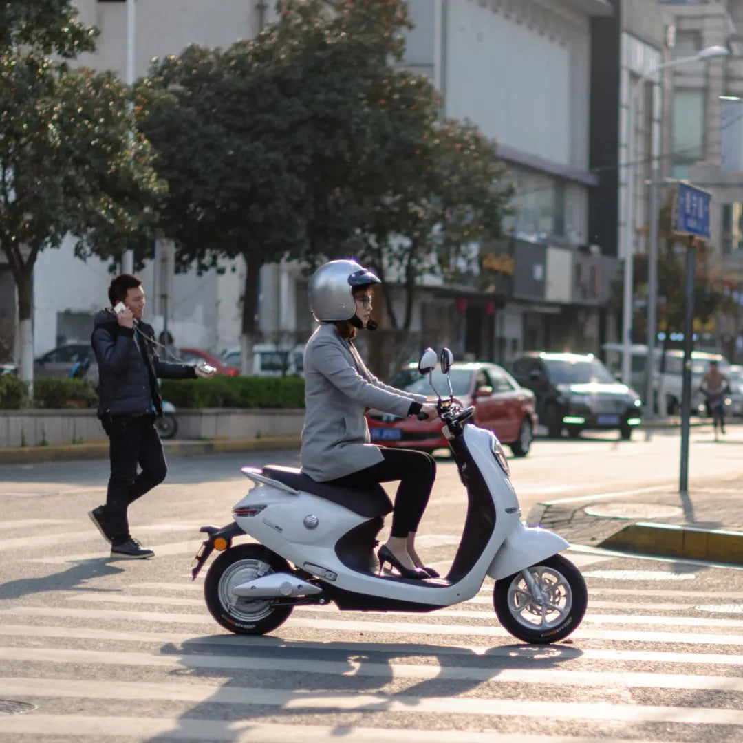 Ženska se vozi z električnim skuterjem Yadea C Umi na prehodu za pešce v mestnem okolju.