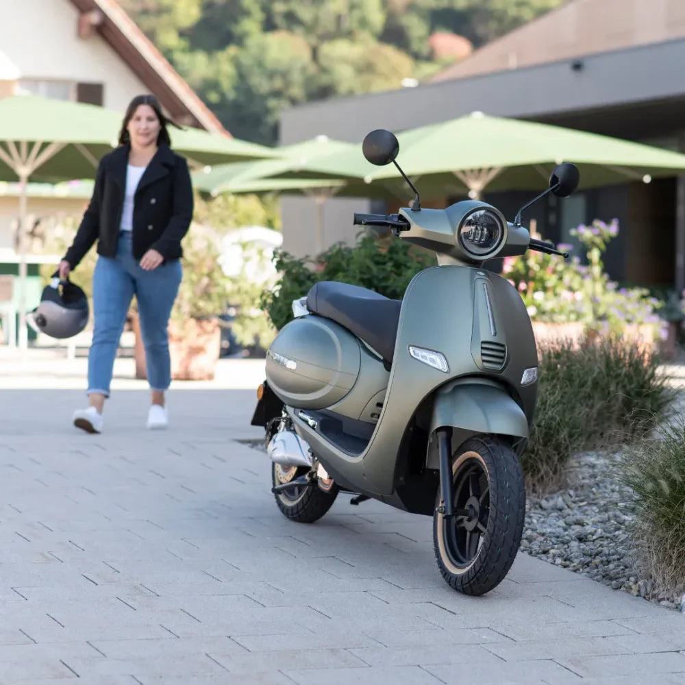 Ženska hodi mimo Električnega skuterja Efo Et5000, parkiranega na elegantni poti.