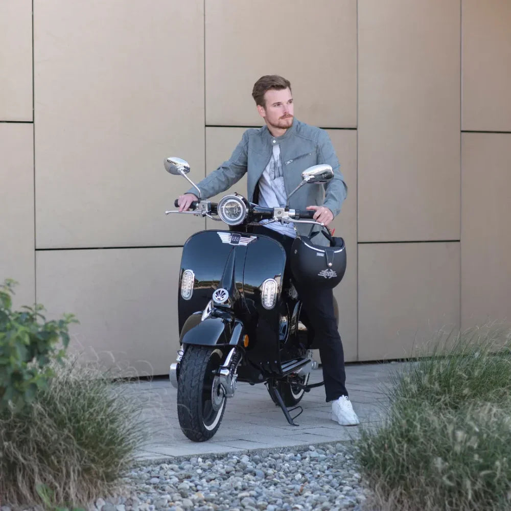 Moški v sivi jakni pozira na električnem skuterju Efo Ev4000 pred moderno kuliso.