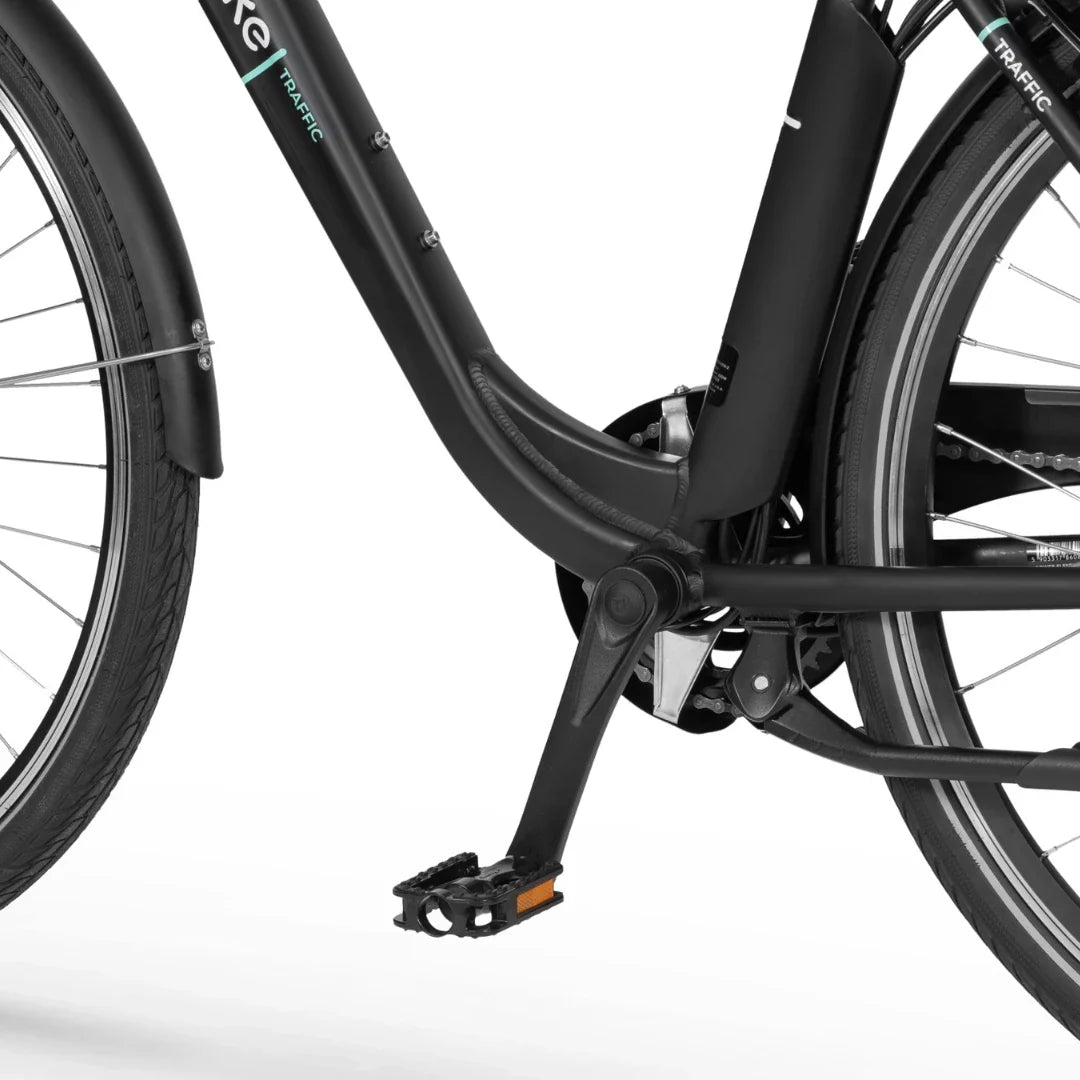 Na sliki je električno kolo znamke Ecobike, model Traffic. Prikazan je del kolesa, vključno s pedalom in okvirjem. Kolo ima črno barvo in je zasnovano za urbano vožnjo, kar nakazuje na njegovo praktičnost in udobje pri vsakodnevni rabi. Vidna je tudi struktura okvirja, ki je prilagojena za stabilnost in enostavno vožnjo.