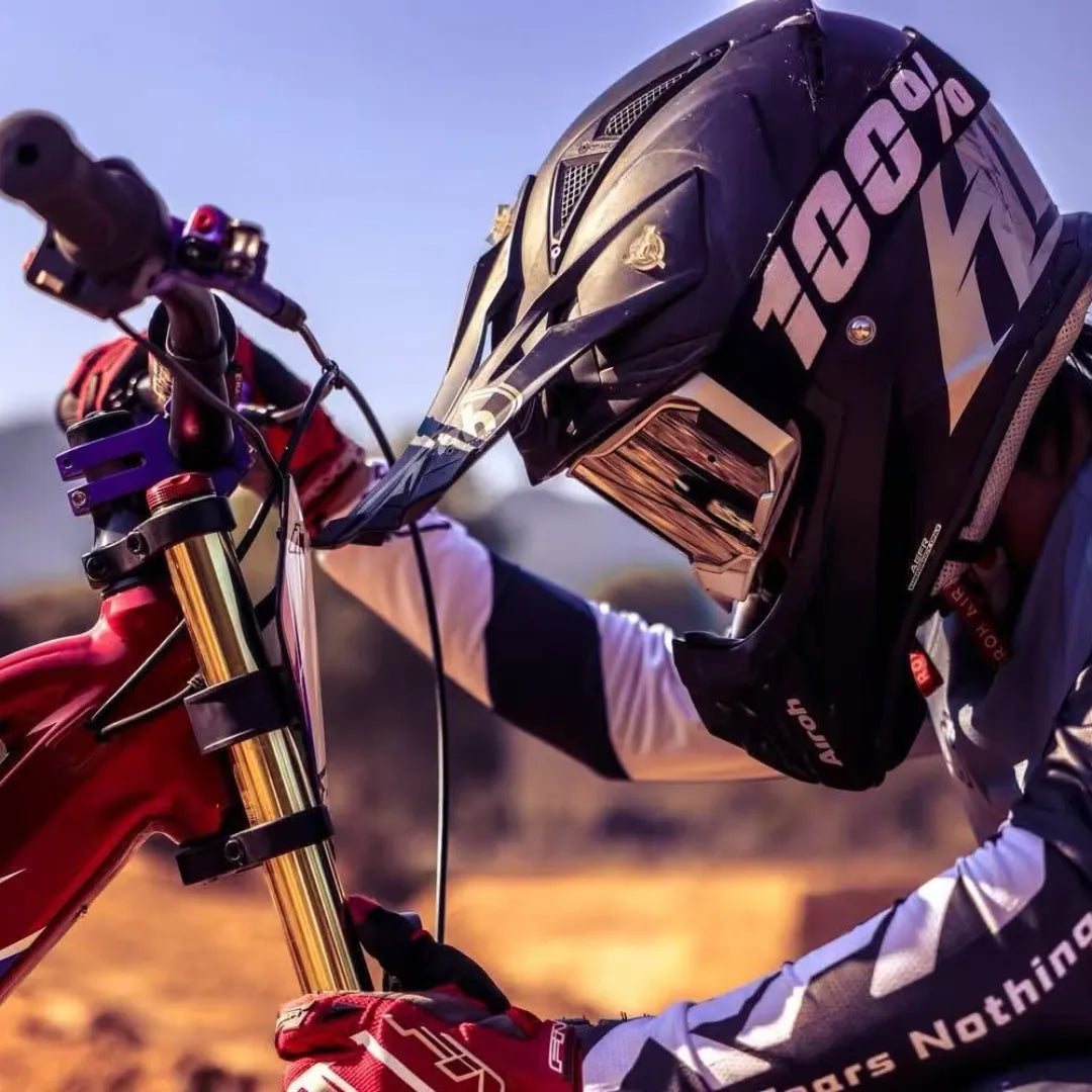 Izdelek je električno kolo, model Apollo Evo Racing 18. Na sliki je vidna oseba v zaščitni čeladi, ki se nagiba nad krmilo kolesa. Kolo ima rdeče in zlato barvo, kar daje športen videz. V ozadju je naravna pokrajina, kar nakazuje na terensko vožnjo.