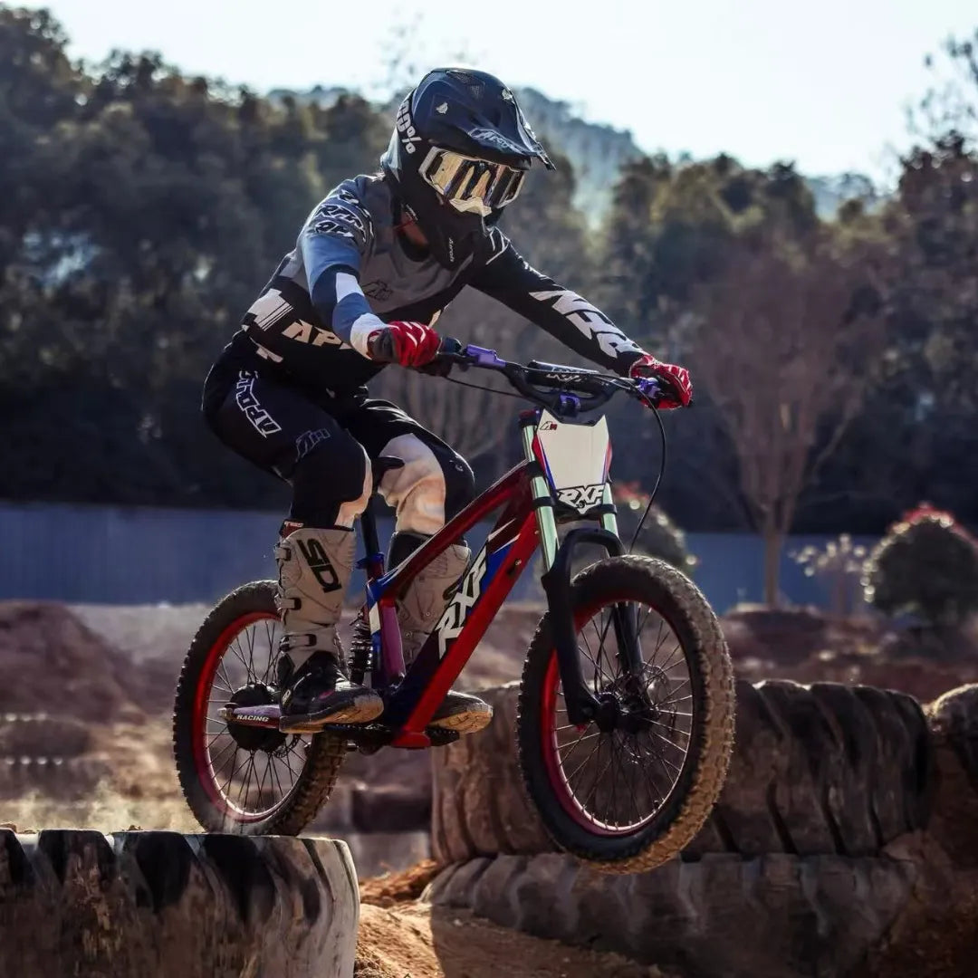 Izdelek je električno kolo, model Apollo Evo Racing 18. Na sliki je prikazan kolesar, ki se vozi po terenski progi in izvaja skok čez oviro. Kolesar nosi zaščitno opremo, vključno s čelado in zaščitnimi hlačami, kar nakazuje na športno in avanturistično naravo uporabe kolesa. Kolo ima robustno zasnovo in je primerno za zahtevnejše terene.