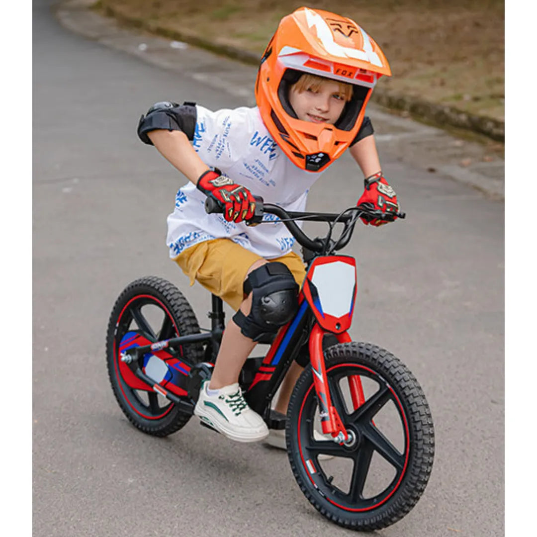 Na sliki je električno kolo, model Apollo Sedna 16 RXF. Vidimo otroka, ki vozi kolo po cesti. Opremljen je s čelado in zaščitnimi blazinicami na komolcih in kolenih, kar kaže na to, da se pripravlja na varno vožnjo. Kolo je v rdeči in črni barvi ter ima široke gume, kar je primerno za vožnjo po različnih površinah.