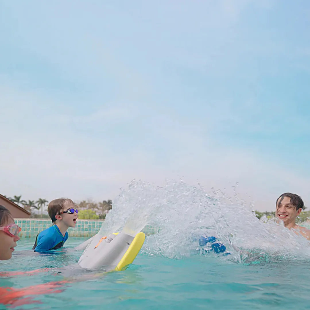 Izdelek na sliki je električna plavalna deska, model Asiwo Mako. Na sliki so vidni otroci v bazenu, ki se zabavajo z desko, ki ustvarja vodne brizge. Otroci nosijo plavalne očala in so oblečeni v kopalne majice, kar nakazuje, da uživajo v vodi. V ozadju je jasno nebo in rastlinje, kar prispeva k sproščenemu vzdušju.