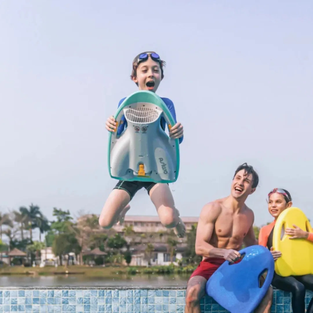 Izdelek na sliki je električna plavalna deska znamke Asiwo, model Mako. Na sliki je videti otroka, ki skače v vodo z električno desko, medtem ko se ob njem smejita dva mladostnika, ki držita druge deske. V ozadju je lepo urejen zunanji prostor ob vodi.