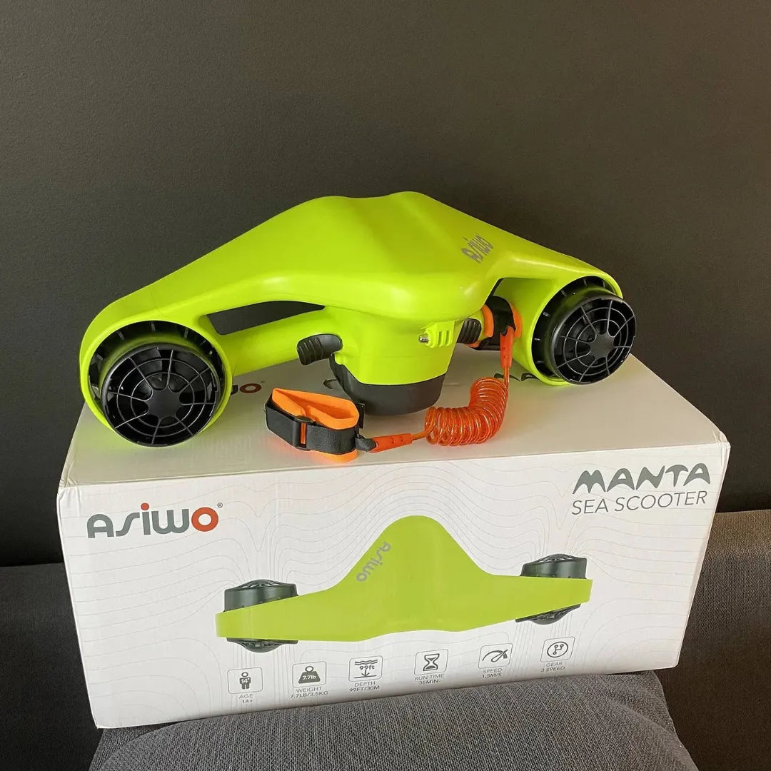 Izdelek na sliki je električni podvodni skuter, model Manta, znamke Asiwo. Na sliki je vidna svetlo zelena naprava z dvema propelerjema, ki je zasnovana za zabavno plavanje pod vodo. Skuter je postavljen na škatlo, ki vsebuje dodatne informacije o izdelku.