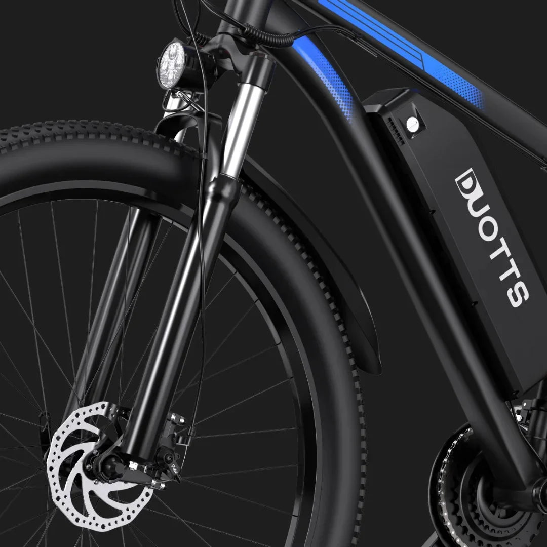 Izdelek je električno kolo znamke DUOTTS, model C29. Na sliki je vidna sprednja vilica kolesa, ki je opremljena s svetilko, ter baterija, nameščena na okvirju. Kolo ima tudi disk zavore, kar nakazuje na boljšo zavorno moč in varnost pri vožnji. Celoten dizajn je sodoben in športen, kar je značilno za električna kolesa.