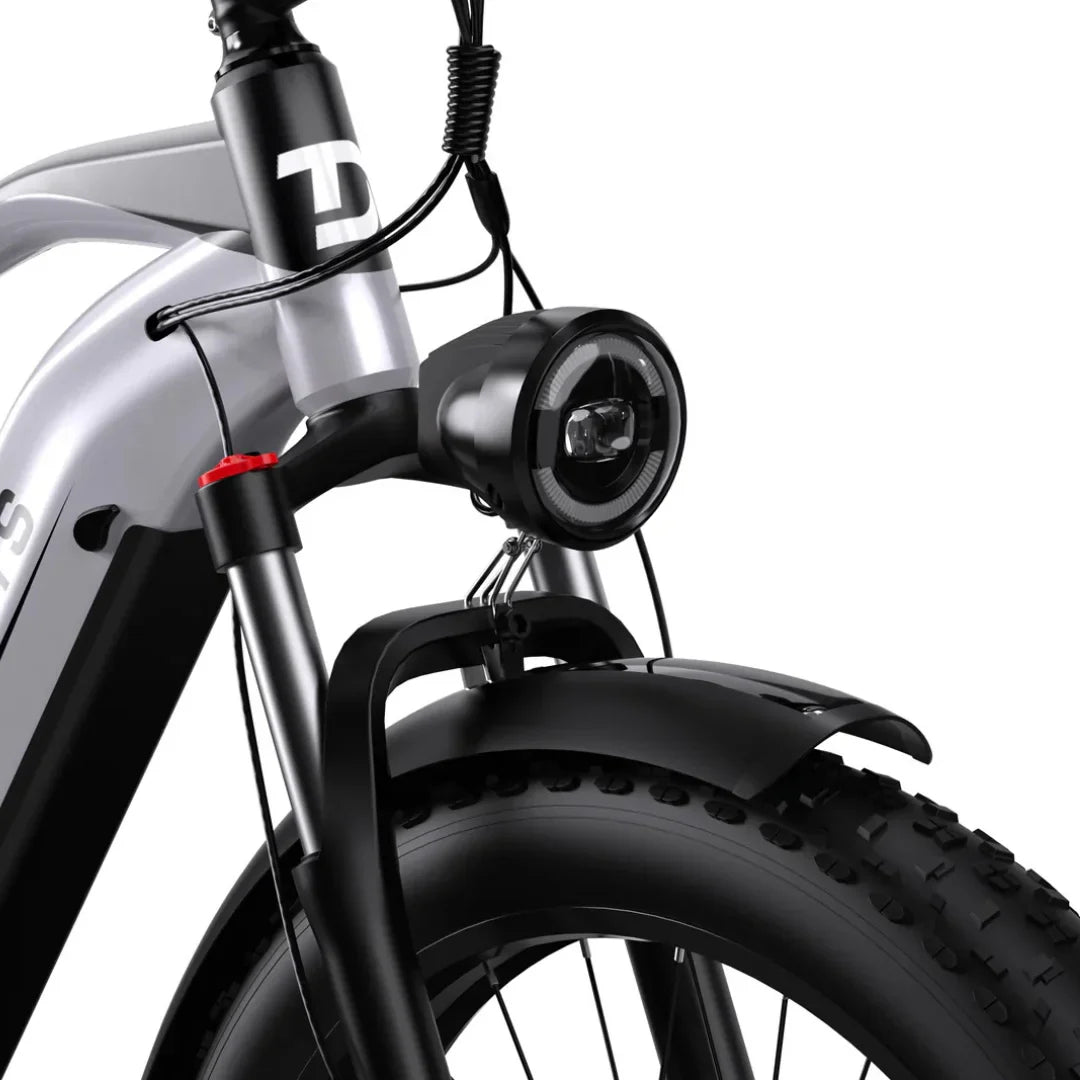 Izdelek je električno kolo, model Duotts F26. Na sliki je prikazan sprednji del kolesa, kjer so vidni okvir, sprednja luč in široka guma z grobim profilom, kar nakazuje na primernost za različne terene. Kolo ima tudi vzmetenje in zaščitni blatnik.