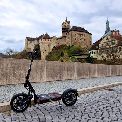 Električni skiro Dualtron City parkiran na tlakovani poti z gradom v ozadju.