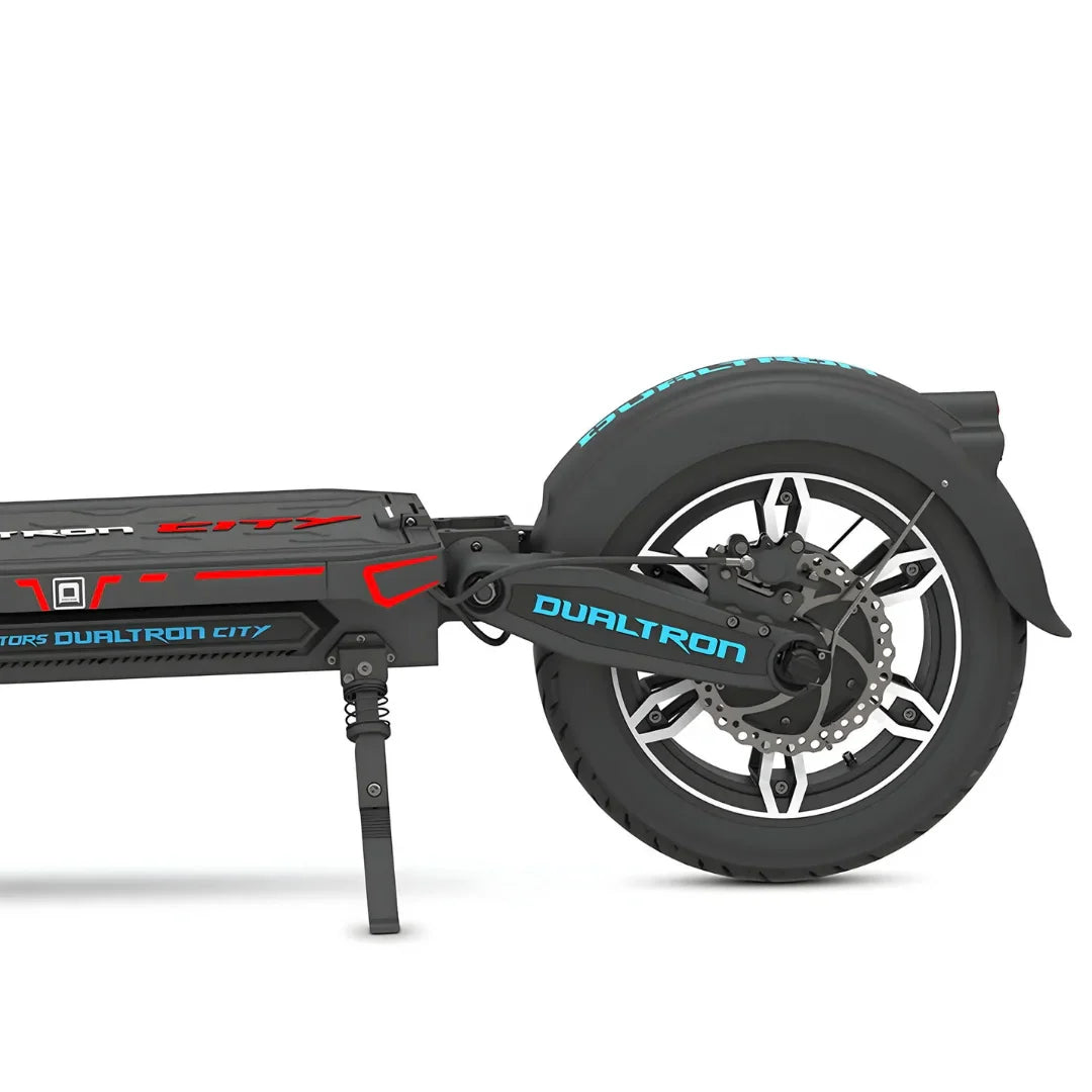 Izdelek na sliki je električni skiro, model Dualtron City. Na sliki je prikazan del skiroja, vključno z zadnjim kolesom, amortizerjem in okvirjem. Kolo ima široko pnevmatiko in disk zavore, kar nakazuje na robustno zasnovo, primerna za mestno vožnjo. Znamka Dualtron je znana po svojih visokokakovostnih električnih skirojih.