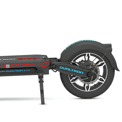 Izdelek na sliki je električni skiro, model Dualtron City. Na sliki je prikazan del skiroja, vključno z zadnjim kolesom, amortizerjem in okvirjem. Kolo ima široko pnevmatiko in disk zavore, kar nakazuje na robustno zasnovo, primerna za mestno vožnjo. Znamka Dualtron je znana po svojih visokokakovostnih električnih skirojih.