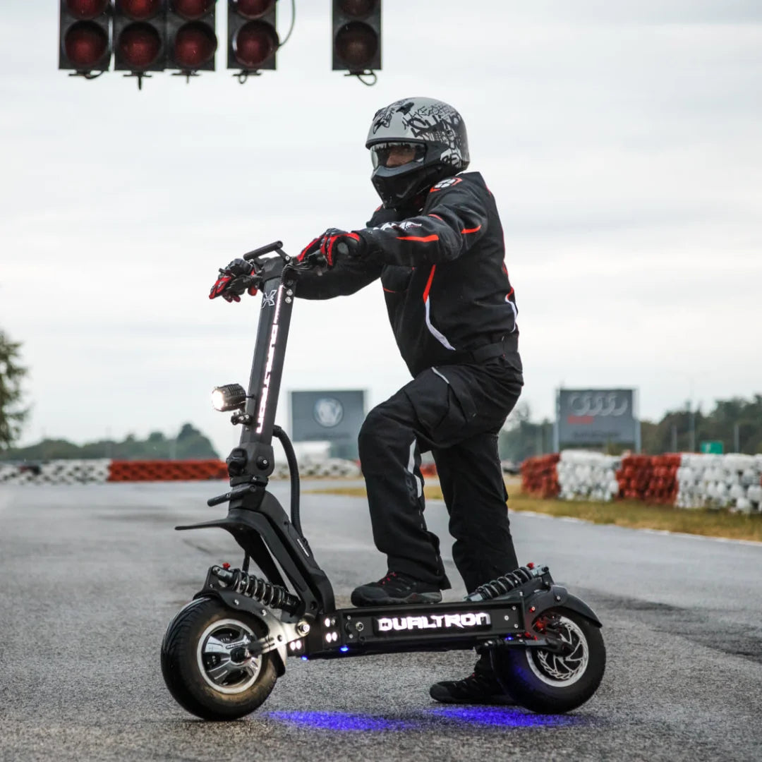 Voznik v opremi stoji na električnem skiroju Dualtron X Limited na dirkališču.