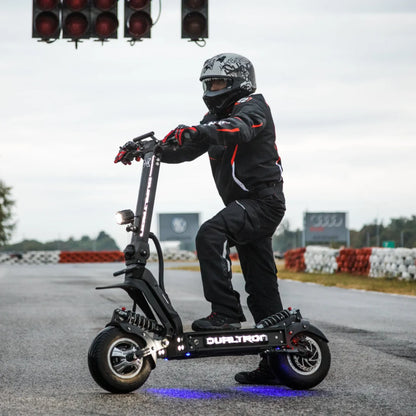 Voznik v opremi stoji na električnem skiroju Dualtron X Limited na dirkališču.
