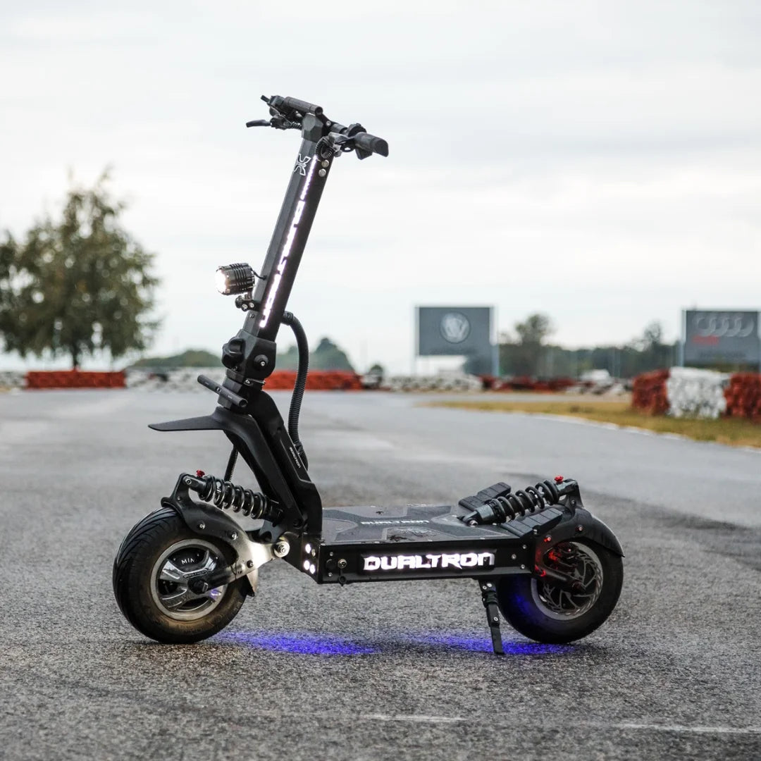 Električni skiro Dualtron X Limited parkiran na dirkališču z oblačnim nebom v ozadju.