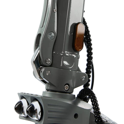 Izdelek je električni skiro, model Eco Speed 10X V2. Na sliki je prikazan del skiroja, ki vključuje mehanizem za zlaganje, svetlobno oznako v oranžni barvi ter dva sprednja reflektorja. Barva skiroja je siva, kar mu daje sodoben videz. Vidna je tudi spiralna zaščita kabla, kar kaže na premišljen dizajn in varnost.