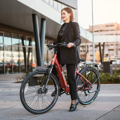 Na sliki je električno kolo znamke Econo, model EER4. Kolo je v rdeči barvi in ima sodoben dizajn. Na sliki je vidna ženska, ki stoji ob kolesu, oblečena v elegantno črno obleko. Okolica je urbana, z modernimi stavbami v ozadju. Kolo ima široke pnevmatike in nosilec za prtljago.