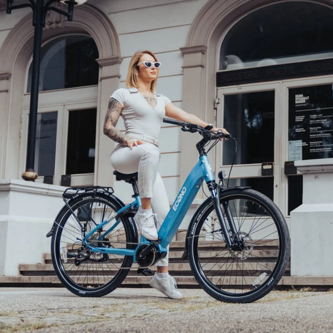 Oseba s sončnimi očali pozira na električnem kolesu Econo Mare City Eec4lk pred stavbo.