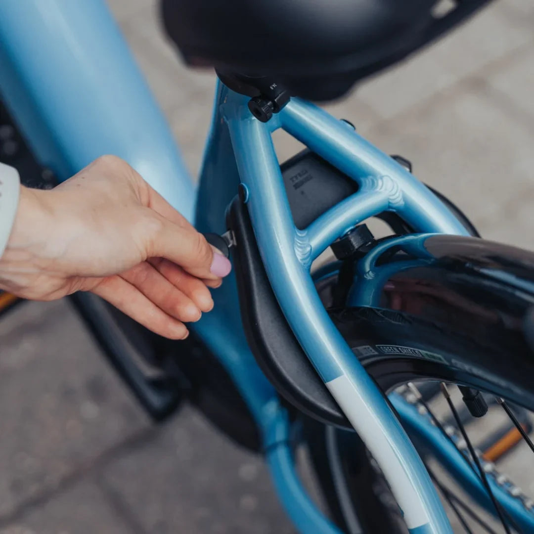 Izdelek je električno kolo, model Econo Mare City EEC4LK. Na sliki je vidna roka, ki drži ključek, ki je povezan z okvirjem kolesa. Kolo ima svetlo modro barvo in je zasnovano za mestno vožnjo, kar nakazuje na njegovo praktičnost in udobje.