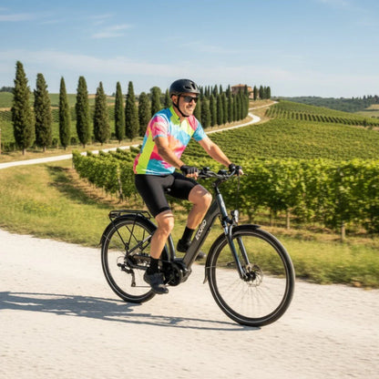 Na sliki je električno kolo znamke Econo, model Mare City. Kolo je opremljeno z električnim motorjem in je zasnovano za mestno vožnjo. Na sliki vidimo kolesarja v barvni majici, ki se vozi po slikoviti poti ob vinogradih, kar nakazuje na prijetno in sproščeno kolesarjenje v naravi.