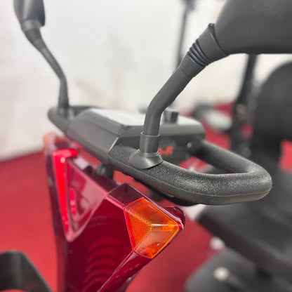 Izdelek na sliki je električni mobilni voziček, model Eco Speed Senior. Vidna je ročica za upravljanje, ki ima ergonomsko obliko, ter del zadnjega dela vozička z odsevniki. Barva vozička je rdeča, kar mu daje privlačen videz. Na sliki je tudi del nadzorne plošče, ki omogoča enostavno upravljanje.