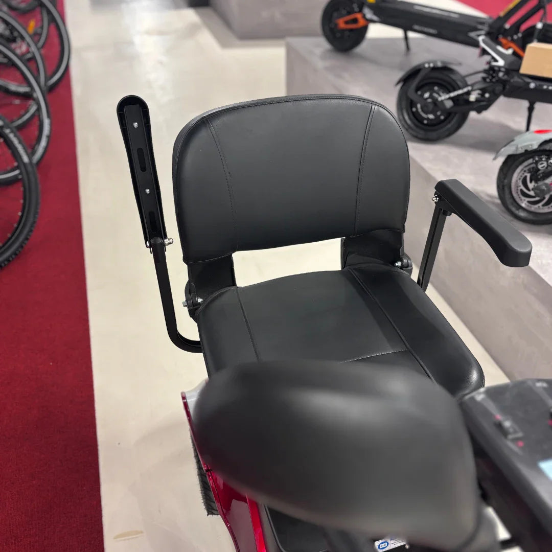 Izdelek je električni mobilni voziček, model Eco Speed Senior. Na sliki je vidna udobna črna sedežna enota z naslonjalom in ročaji, kar nakazuje na zasnovo, prilagojeno starejšim uporabnikom. V ozadju so vidni drugi električni skiroji in kolesa, kar kaže na prodajno okolje.