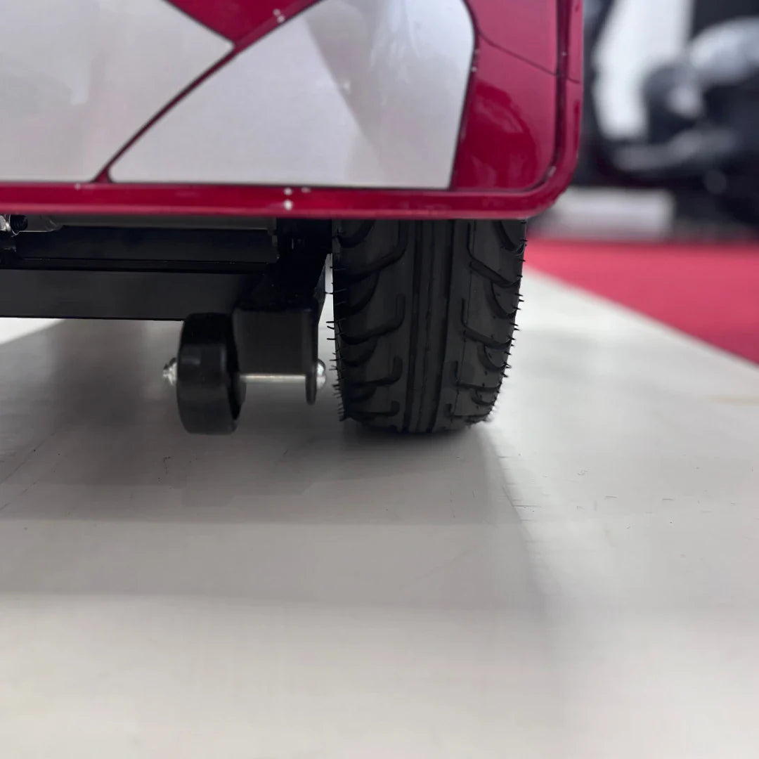 Izdelek je električni mobilni voziček, model Eco Speed Senior. Na sliki je vidna podrobnost zadnjega kolesa vozička, ki ima gumirano pnevmatiko z dobro oprijemljivostjo. Oprema je zasnovana za udobno in varno vožnjo, kar je pomembno za starejše uporabnike. V ozadju je del okolice, kar nakazuje, da je voziček postavljen v razstavnem prostoru.
