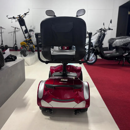 Izdelek je električni mobilni voziček, model Eco Speed Senior. Na sliki je vidna zadnja stran vozička, ki ima udoben sedež in ročaje. Voziček je v rdeči barvi, s svetlečimi belimi detajli. V ozadju so vidni tudi drugi električni skiroji in vozila, kar nakazuje, da gre za prodajno mesto s široko izbiro električnih prevoznih sredstev.