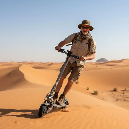 Na sliki je električni skiro, model Eco Speed 10X V2. Zasnova skiroja je moderna in robustna, kar je vidno v njegovi konstrukciji. Oseba, ki ga vozi, je oblečena v udobna oblačila za aktivnosti na prostem, kar nakazuje na avanturistično naravo uporabe skiroja. Ozadje prikazuje peščene sipine, kar dodatno poudarja, da je skiro primeren za vožnjo v različnih terenih.