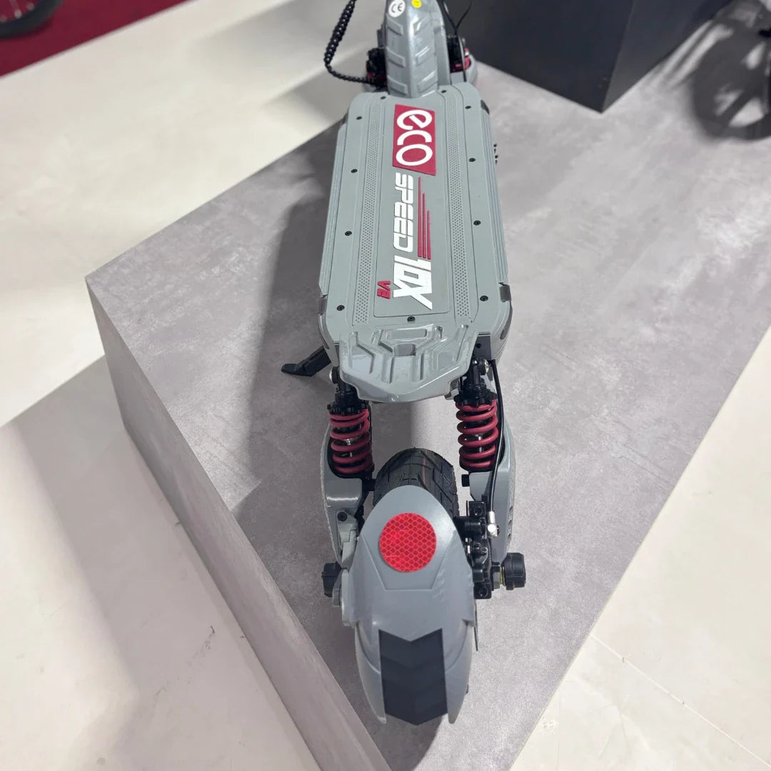 Izdelek na sliki je električni skiro, model Eco Speed 10X V2. Na sliki je vidna njegova zasnova z jasno označeno znamko, robustno ploščo in vzmetenjem na zadnjem delu. Skir je opremljen z velikim zadnjim kolesom in reflektorjem, kar prispeva k varnosti med vožnjo. Celoten videz nakazuje na trpežnost in zmogljivost.