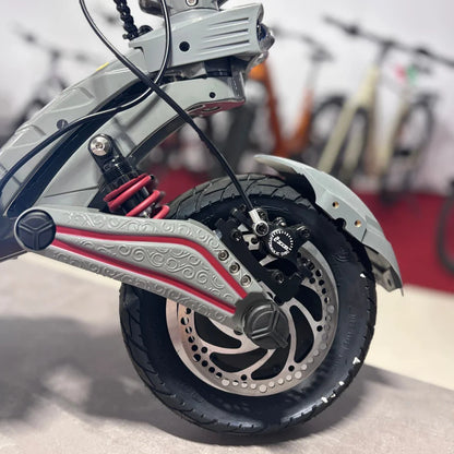 Izdelek na sliki je električni skiro, model Eco Speed 10X V2. Na sliki je prikazana stran skiroja, kjer so vidni detajli, kot so amortizer, kolo z disk zavornim sistemom ter dekorativni elementi na okvirju. V ozadju so vidni tudi drugi skiroji, kar nakazuje, da gre za prodajno mesto ali razstavo.